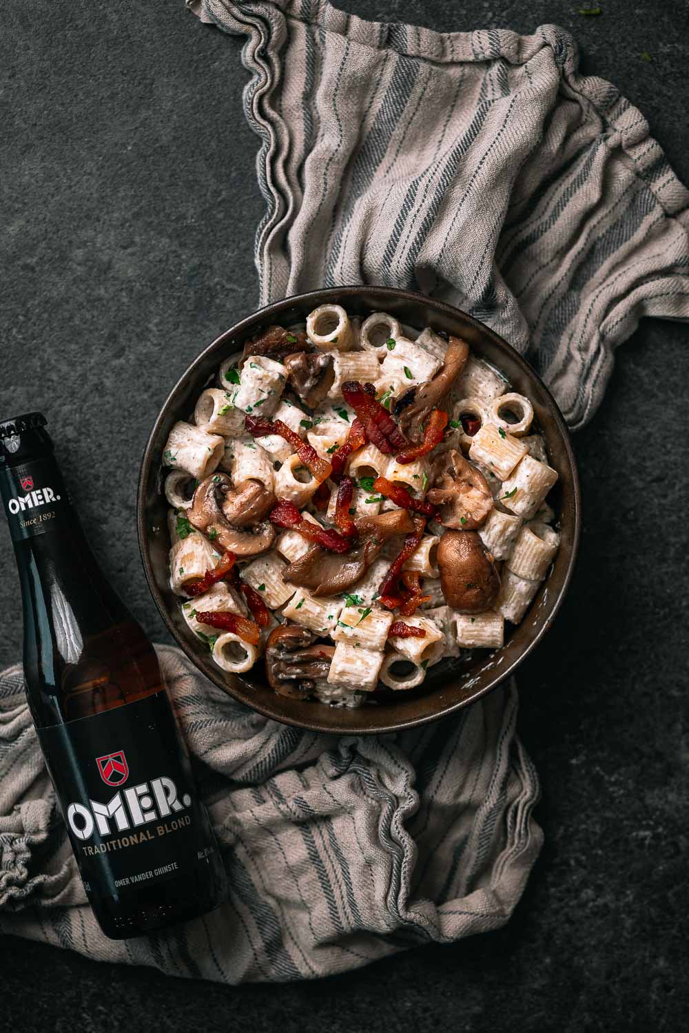 Pasta rigatoni met guanciale en een flesje OMER. bier er naast