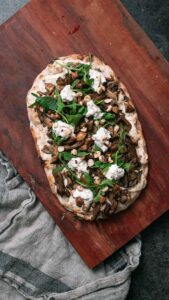 Herfstige Pinsa met champignons en truffel op ene houten plaat met een stoffen doekje eronder